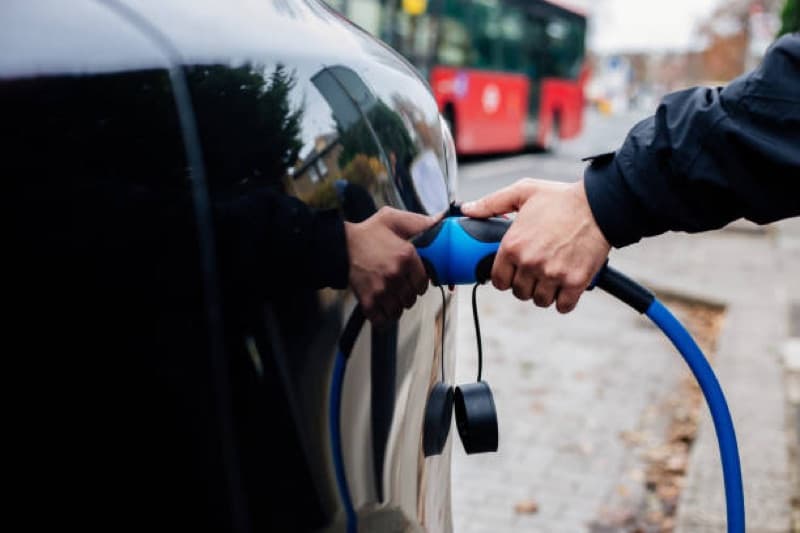 An electric car being plugged in beside a London bus